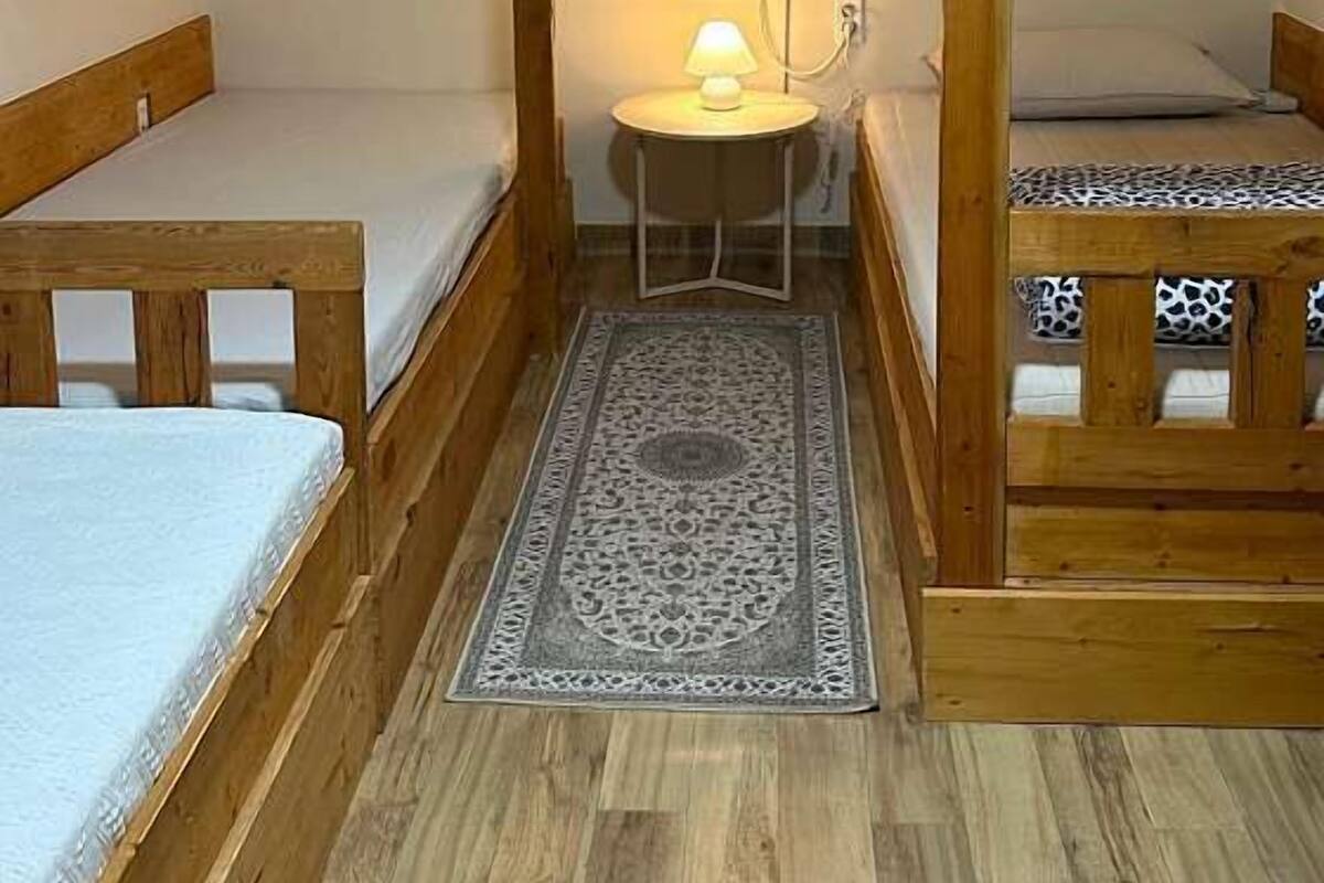 Een kleine, compacte kamer met een stapelbed, een enkel bed en een klein tafeltje met een lamp.