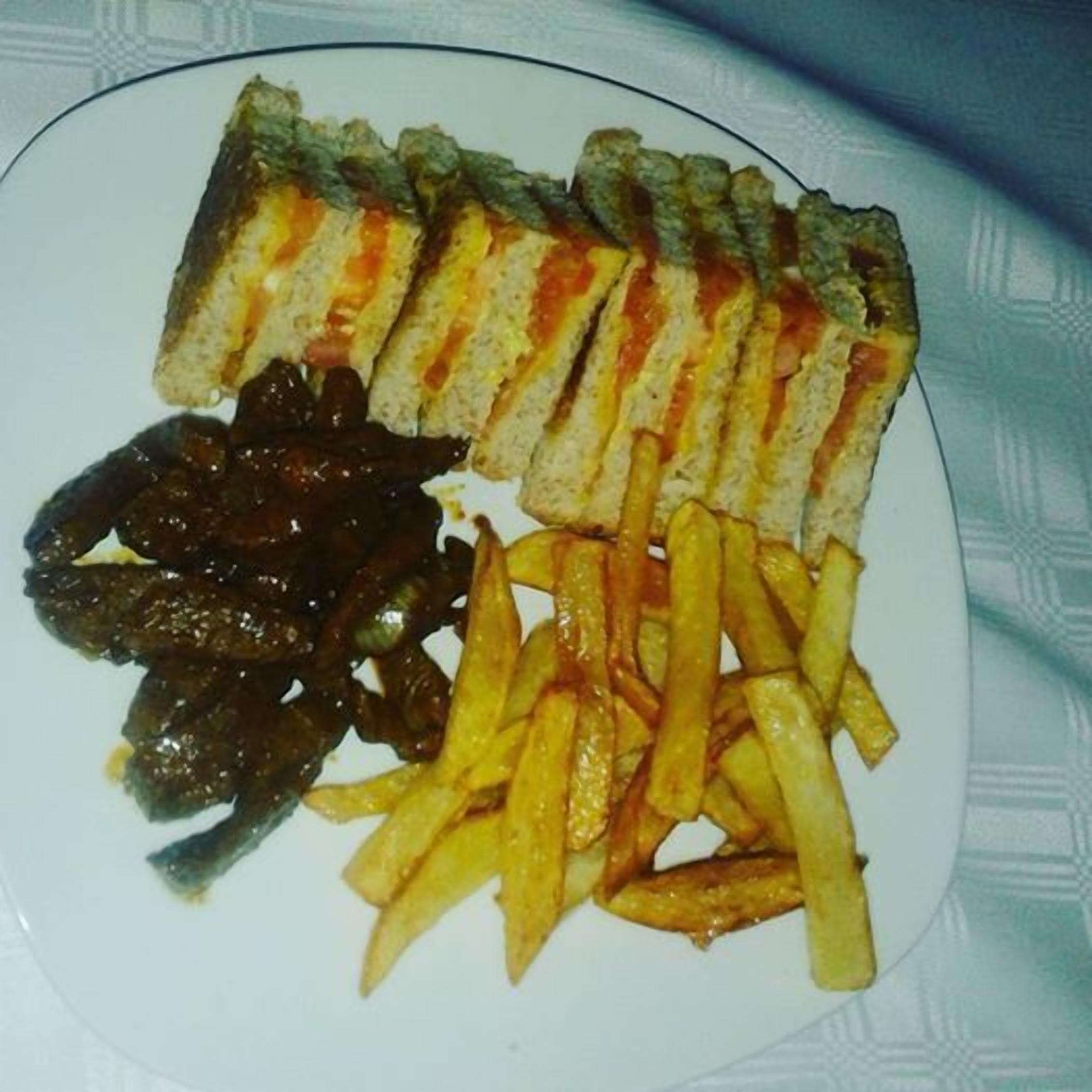 Un plat amb un entrepà, patates fregides i una salsa fosca.