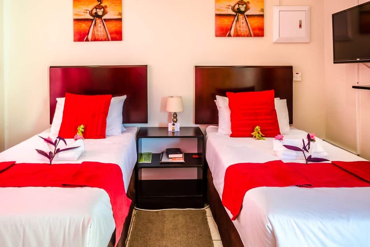 Une chambre d’hôtel avec deux lits, chacun agrémenté de draps rouges et blancs, une table de chevet avec une lampe et des œuvres d’art accrochées aux murs.