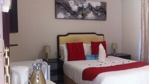 A hotel room with a bed, two bedside tables, a lamp, a painting on the wall, and a window with curtains.
