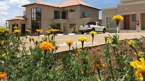 A building with a tiled roof, a white pickup truck parked in front, and yellow flowers in the foreground.