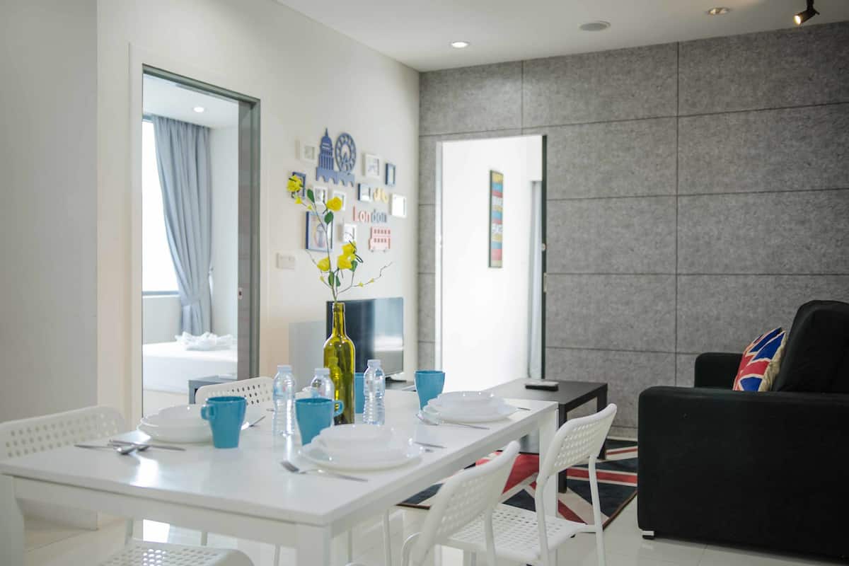 A dining area with a white table set for four, a vase with yellow flowers, and a wall with framed pictures and a clock.