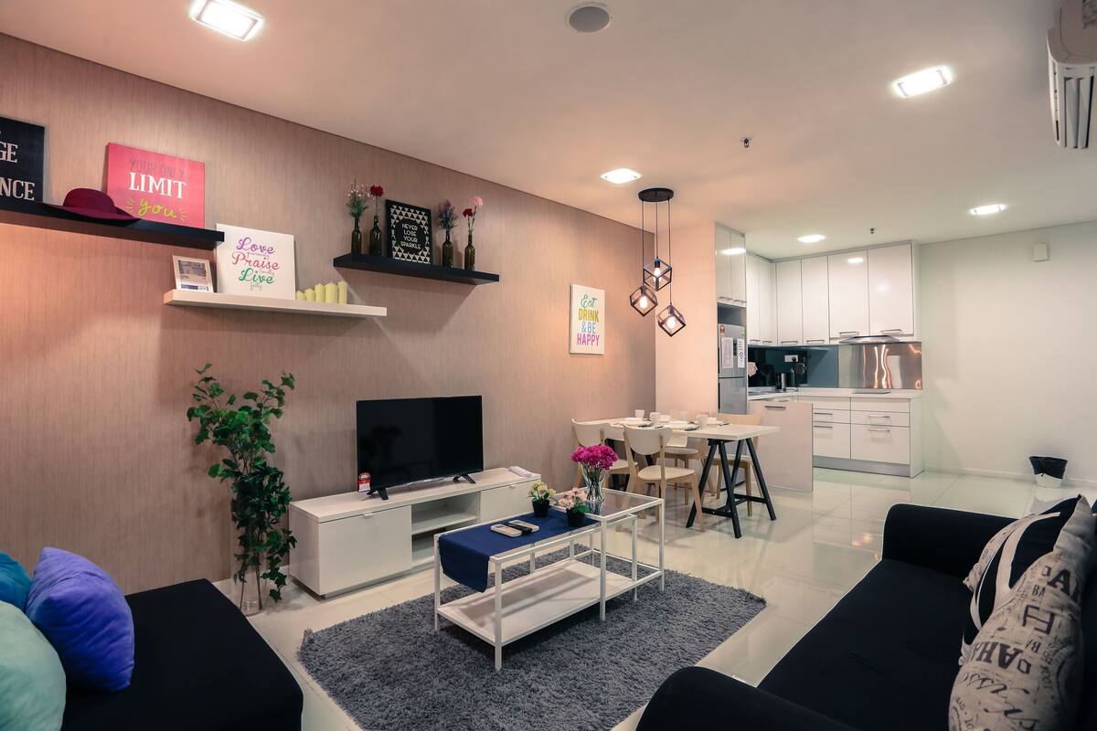 A modern living room with a TV, sofa, coffee table, and decorative items. A kitchen is visible in the background.