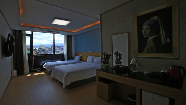 A hotel room with two beds, a desk with a mirror, a painting, and a view of the city.