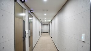 A long, narrow hallway with lockers on both sides, a carpeted floor, and a ceiling with recessed lighting.