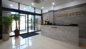 A hotel reception area with a marble counter, potted plants, and a clear view of the outside.