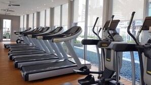 A gym with multiple treadmills and elliptical machines, large windows, and a wooden floor. - Vortex Suite KLCC at Penguin Homes (Kuala Lumpur)