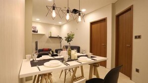 A dining area with a white table set for four, wooden chairs, and pendant lighting. - Vortex Suite KLCC at Penguin Homes (Kuala Lumpur)