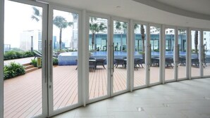 A spacious indoor area with large glass doors leading to an outdoor deck with seating and a pool. - Vortex Suite KLCC at Penguin Homes (Kuala Lumpur)