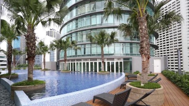 A modern hotel with a circular infinity pool, palm trees, and a wooden deck with lounge chairs. - Vortex Suite KLCC at Penguin Homes (Kuala Lumpur)