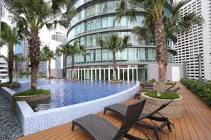 Ein modernes Hotel mit einem kreisförmigen Infinity-Pool, Palmen und einer Holzterrasse mit Liegestühlen.