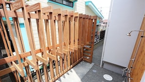 A wooden gate leading to a building with a visible water spout and a metal grate on the ground. - Shonan-Enoshima Seaside Guest House – Hostel (Fujisawa)