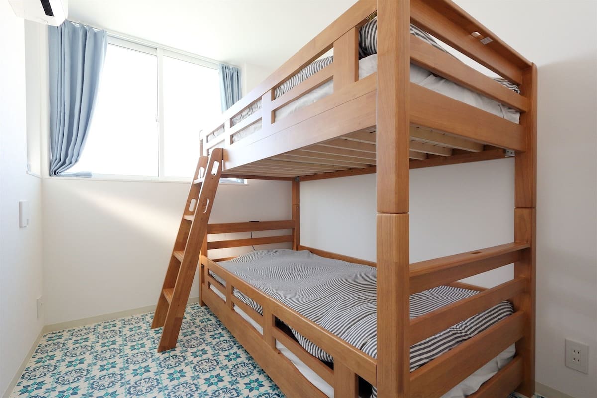 Un lit superposé avec une échelle en bois, une fenêtre avec des rideaux et des carreaux de sol à motifs.