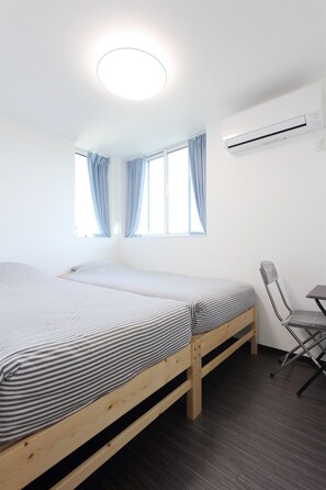 A room with two beds, a desk, and an air conditioning unit.