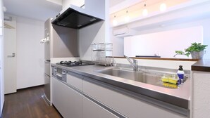 A modern kitchen with a stainless steel sink, a black range hood, and a built-in dishwasher. - Shonan-Enoshima Seaside Guest House – Hostel (Fujisawa)