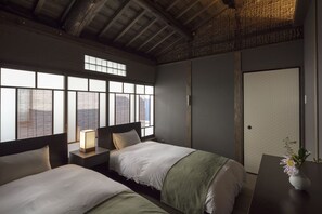 Traditional hotel room with two beds, a bedside table, and a large window offering a city view.