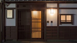 En traditionel japansk bygning med en træport, et lille vindue og en udvendig lysarmatur.