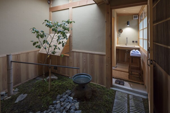 A traditional Japanese-style bathroom with a wooden interior, a small garden area with a tree, and a stone basin.