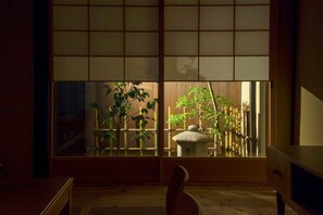A traditional Japanese room with tatami flooring, a low wooden table, and a sliding shoji screen with a view of bamboo plants and a stone lantern.