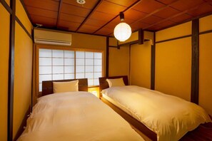 A traditional Japanese-style room with two single beds, a shoji screen window, and a ceiling fan.