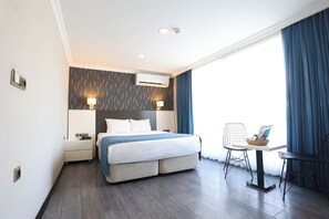 A hotel room with a bed, bedside lamps, a desk with a chair, and a window with curtains. - Riva Hotel Alsancak (Izmir)