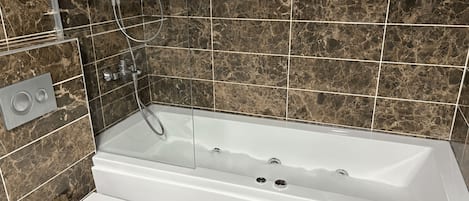Casa de banho com banheira branca, sanita e dispensador de sabonete líquido na parede.
