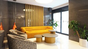 A modern living room with a yellow sofa, patterned armchairs, and a coffee table. - Riva Hotel Alsancak (Izmir)
