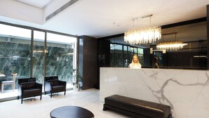 A modern reception area with a marble reception desk, black leather sofas, and a large chandelier. - Riva Hotel Alsancak (Izmir)
