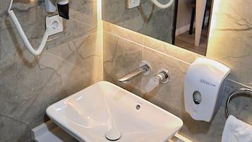 A bathroom with a white sink, a handheld hair dryer, a towel rack, and a soap dispenser.