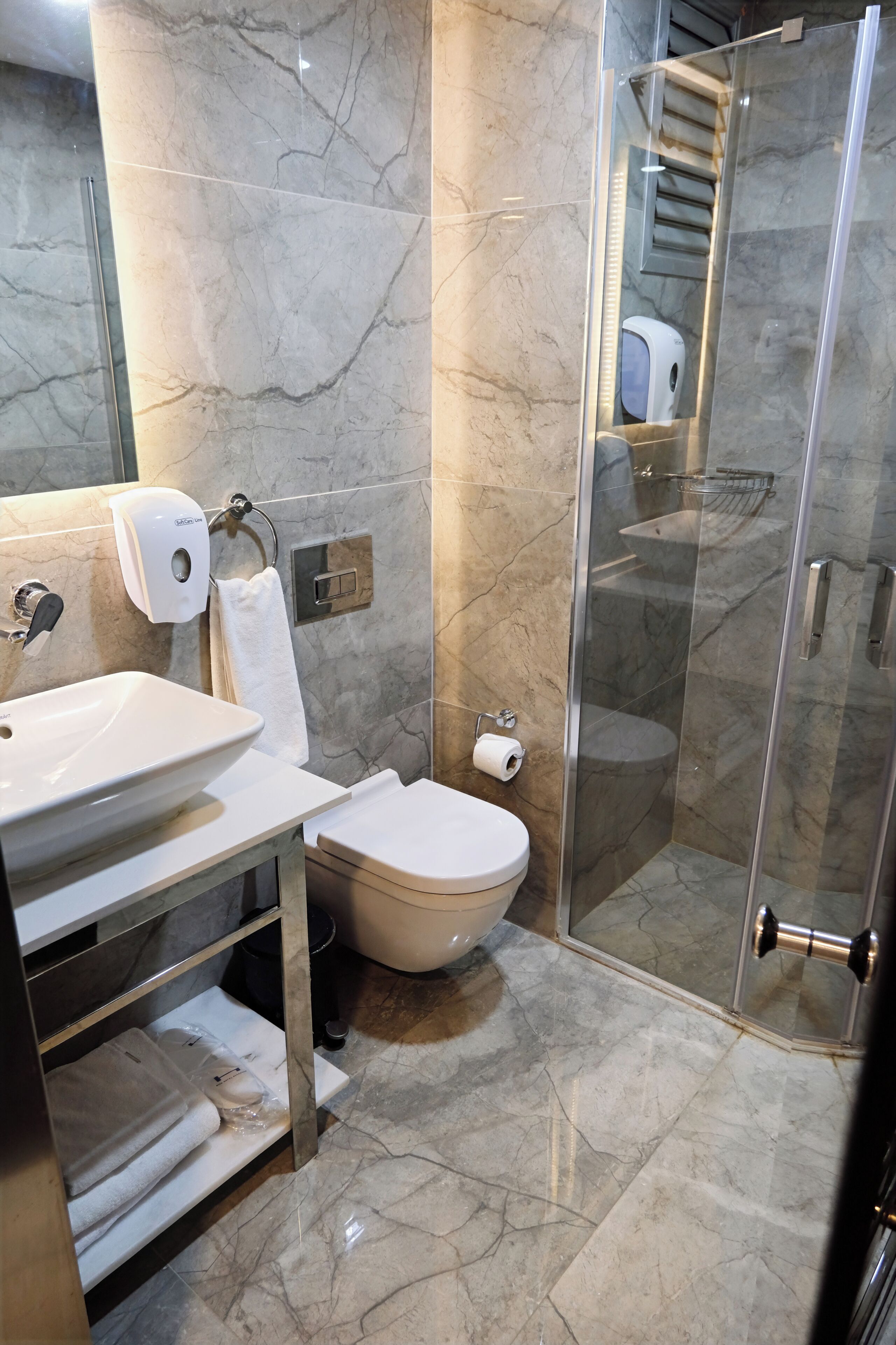 Un bagno moderno con pavimento in marmo, box doccia in vetro, lavabo bianco e un water.