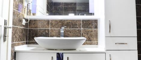 Un baño con lavamanos blanco, un espejo encima y armarios abajo.