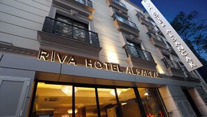 The exterior of Riva Hotel Alanzale with illuminated signage, large windows, and a balcony with decorative railings. - Riva Hotel Alsancak (Izmir)