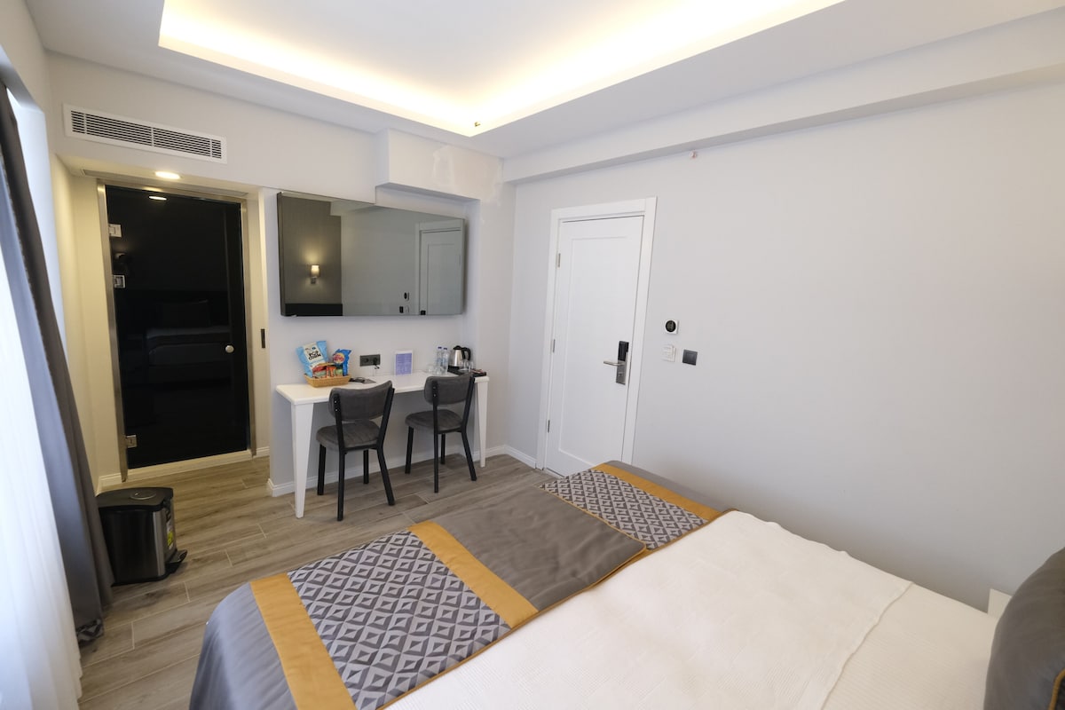 A hotel room with a bed, a desk, two chairs, a small kitchenette, and a door.