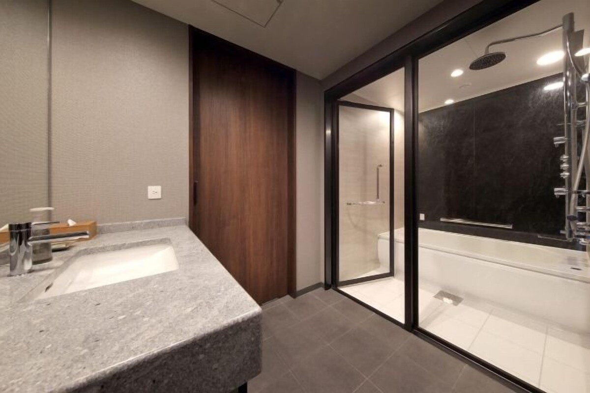 Un baño moderno con lavamanos de granito, pared de acento de madera y zona de ducha con mampara de vidrio.