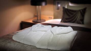A neatly folded white towel on a textured brown chair in a dimly lit room with a lamp and a pillow on the bed.