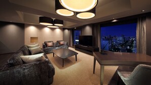 A modern living room with a sofa, coffee table, and TV, featuring a city view through large windows.