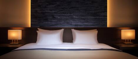 A large bed with a dark headboard, two bedside lamps, and a textured wall behind.