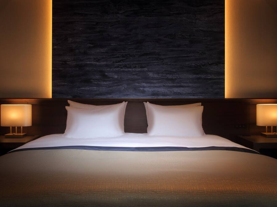 Una cama grande con cabecera oscura, dos lámparas de noche y una pared con textura.
