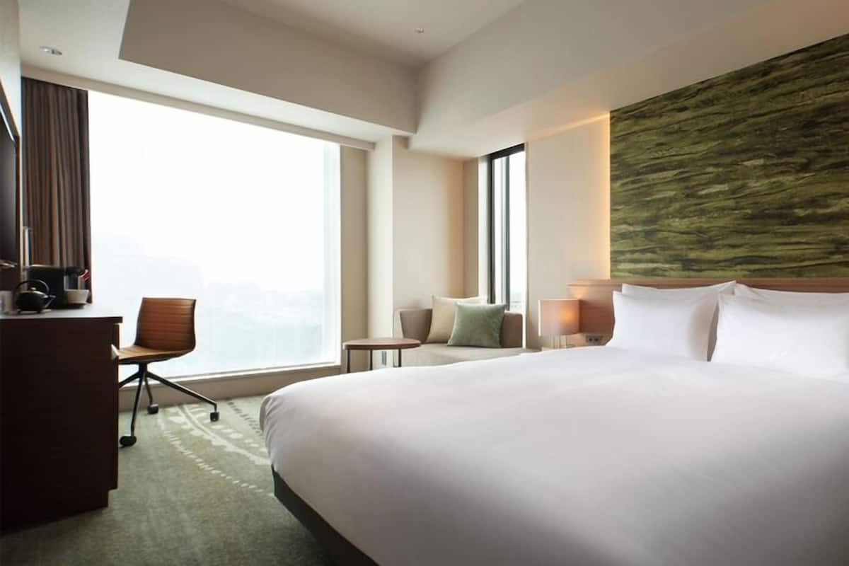 Une chambre d’hôtel avec un grand lit, un bureau, une chaise, une petite table et une vue sur la ville.