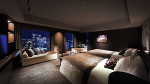 Habitación de hotel moderna con una cama grande, un sofá y un televisor. La habitación ofrece vistas a la ciudad a través de amplias ventanas.