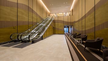 An indoor area with an escalator, seating, and a corridor.