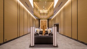 A modern hotel lobby with a central seating area, a decorative wooden sculpture, and a high ceiling with recessed lighting.