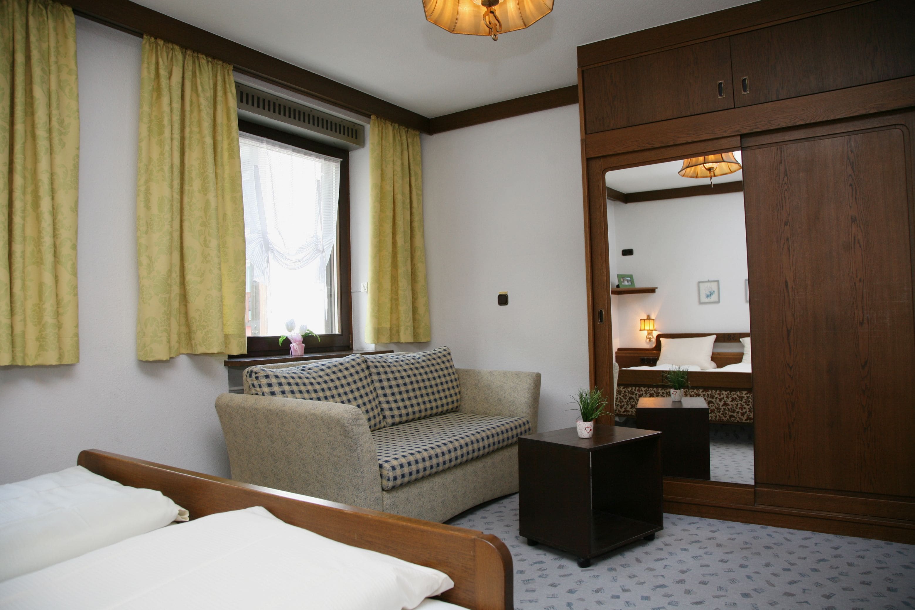Une chambre d’hôtel avec un lit, un canapé, une petite table, une armoire et une fenêtre avec des rideaux.