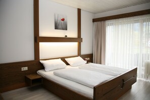 A double bed with wooden headboard and footboard, two bedside tables, a nightstand, and a wall-mounted light fixture. - Hotel Pflug Ottenhöfen (Ottenhofen im Schwarzwald)