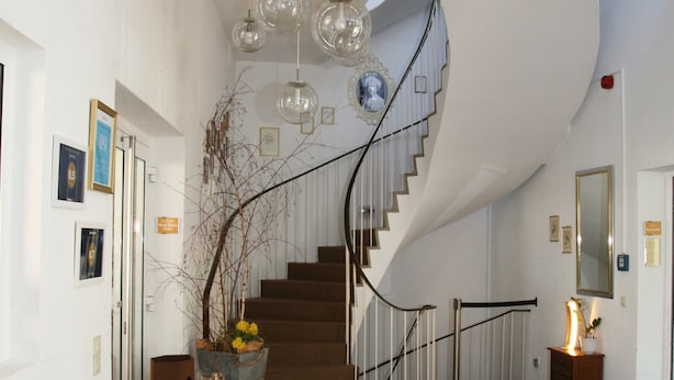 A modern interior with a curved staircase, a sofa with cushions, and hanging light fixtures. - Hotel Pflug Ottenhöfen (Ottenhofen im Schwarzwald)