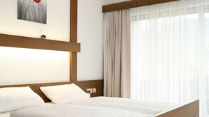 A bedroom with a wooden bed, white bedding, a nightstand, a lamp, a painting on the wall, and a window with curtains. - Hotel Pflug Ottenhöfen (Ottenhofen im Schwarzwald)