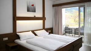 A hotel room with a large bed, a small table and chairs, a painting on the wall, and a balcony with a view of trees. - Hotel Pflug Ottenhöfen (Ottenhofen im Schwarzwald)