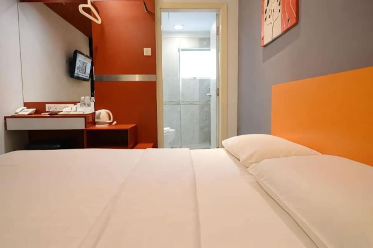 A hotel room with a bed, a desk, a chair, and a shower area.