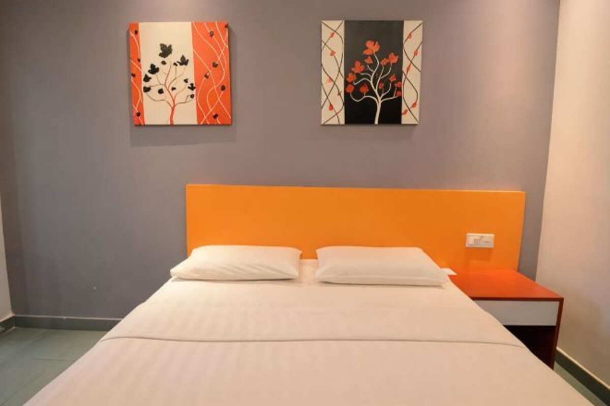 A hotel room with a bed, two paintings on the wall, and a nightstand.
