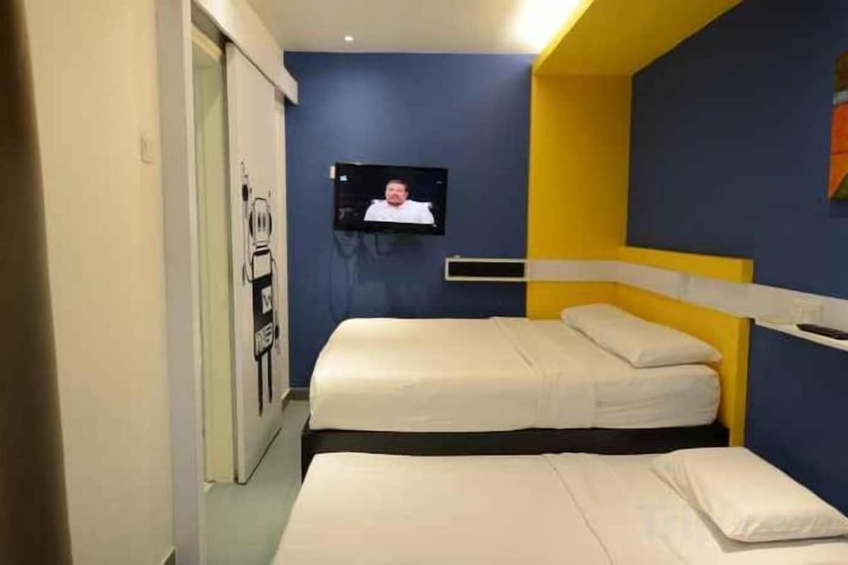 A hotel room with two beds, a television mounted on the wall, and a door with a poster.